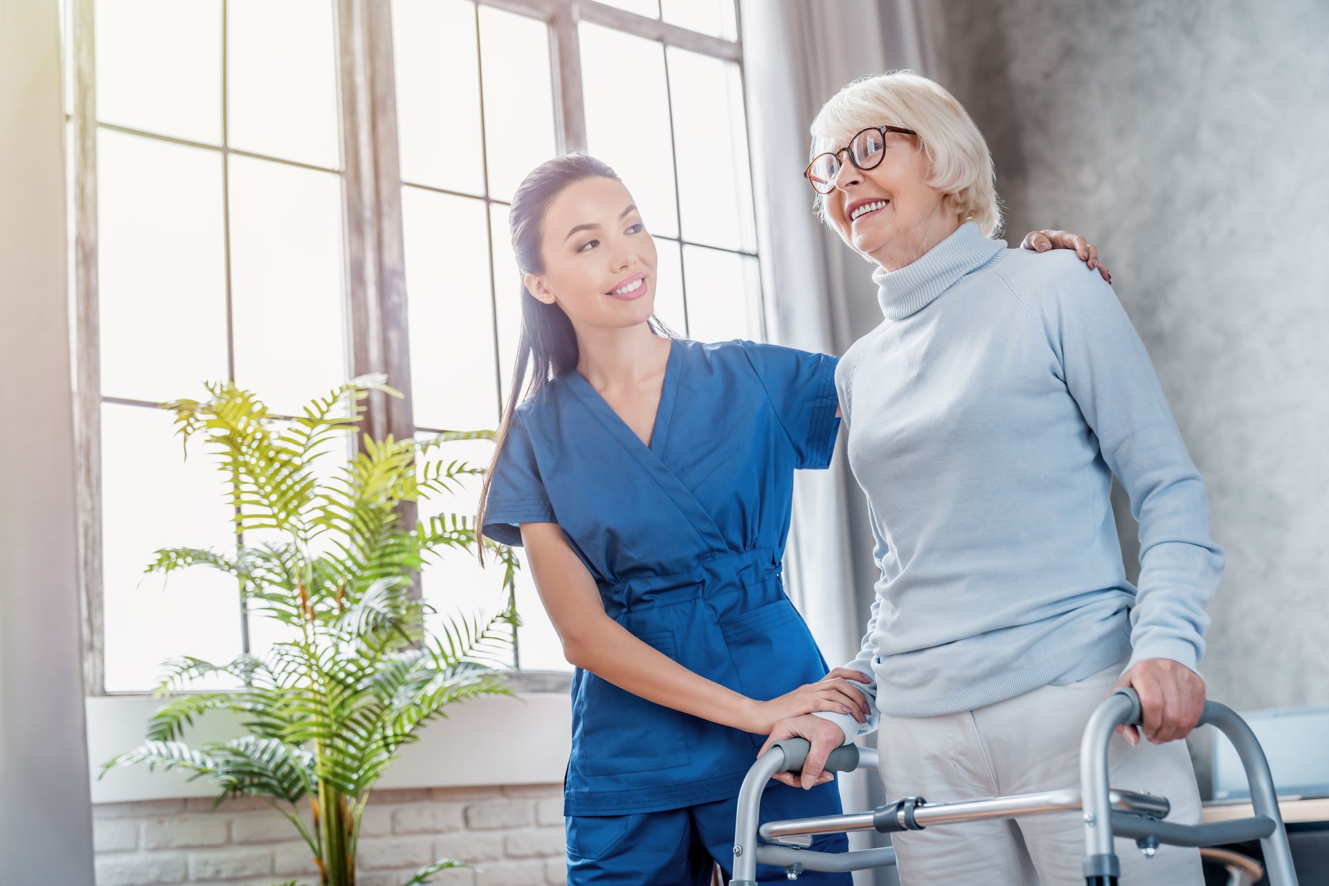 Female asian nurse helping senior woman to walk with walker at home